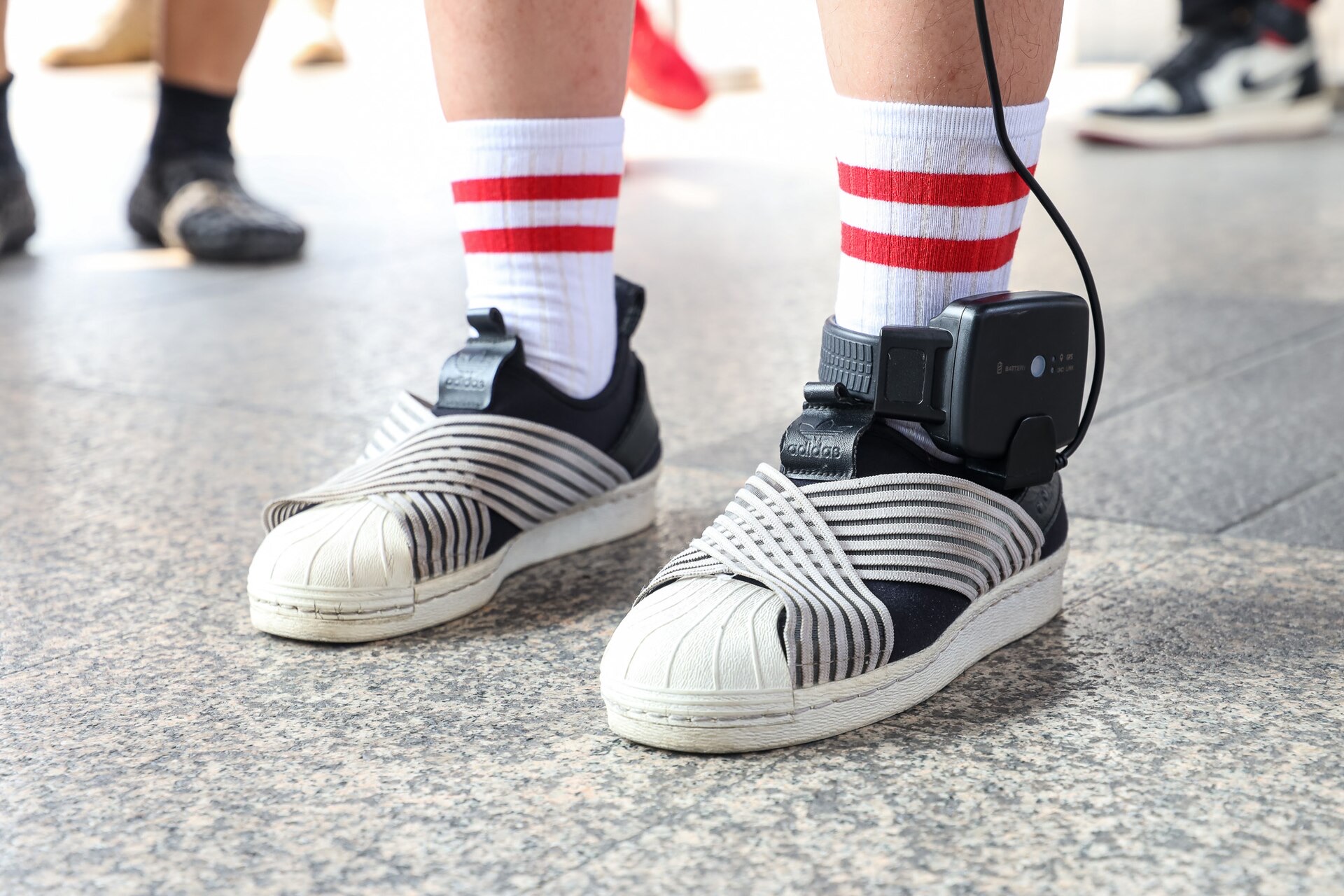 A GPS electronic monitoring bracelet strapped above a sneaker on a person's ankle
