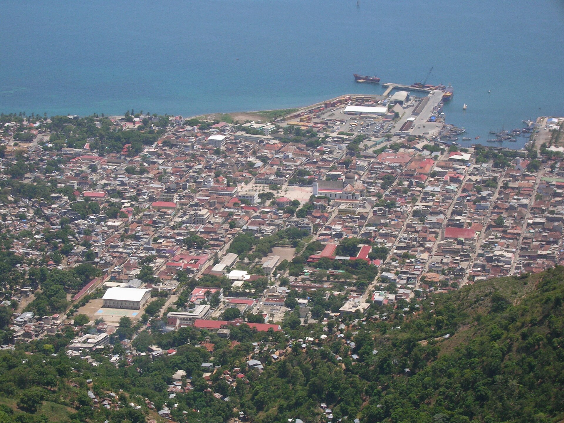 Cap-Haïtien seen from the hillside of Morne Jean — dense city blocks, the cathedral dome, and the harbour with cargo ships at the pier