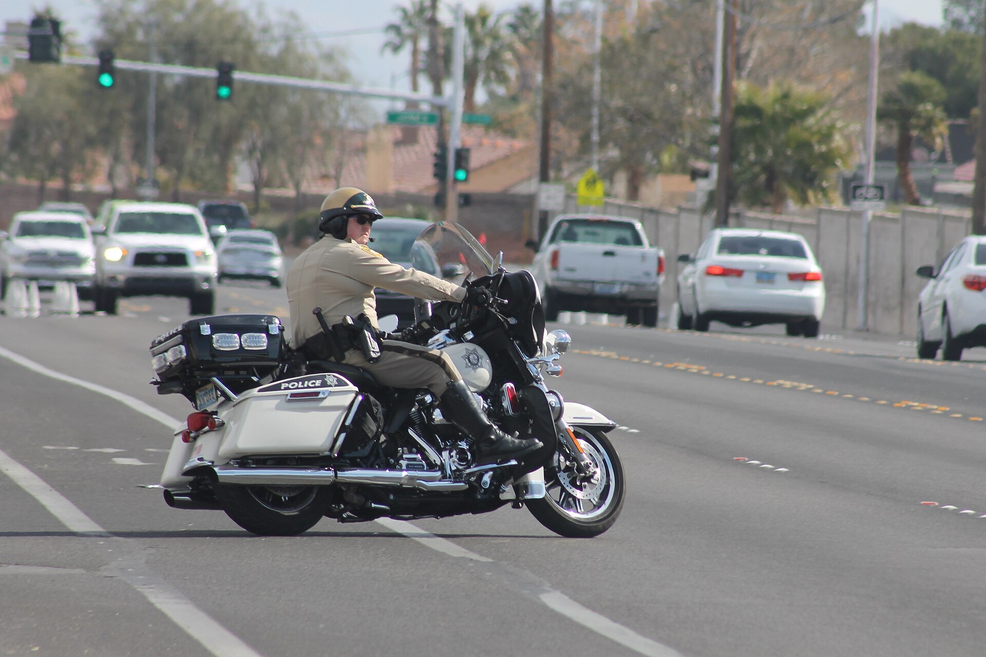 A motorcycle police officer in a helmet and tan uniform at the roadside, about to begin a traffic stop